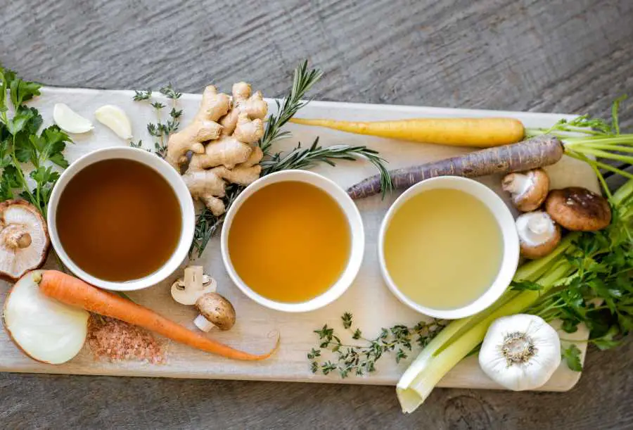 three cups of bone broth with some vegetables on a white board