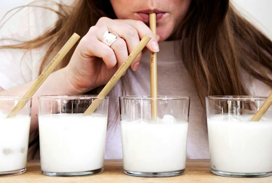 A woman testing milk with a straw from four glasses of milk