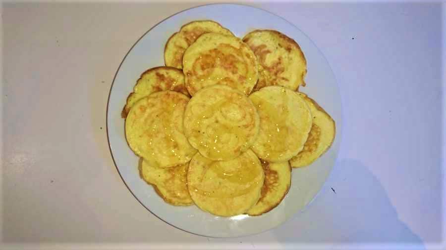 Cooked mini pancakes drizzled with honey on a plate