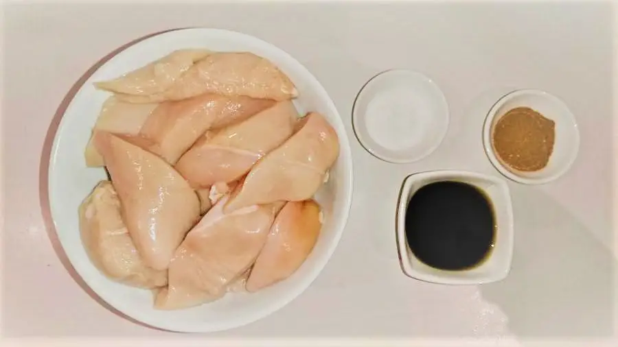 a bowl of raw chicken and three small bowls of spices