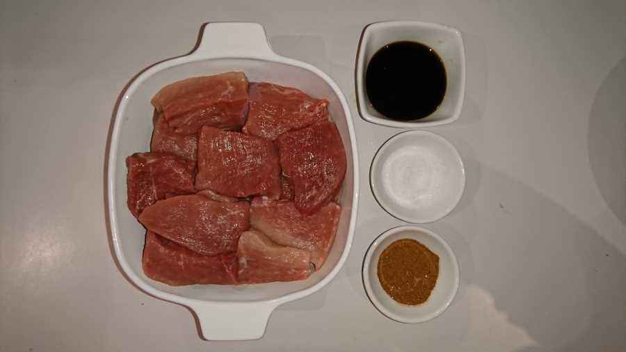 A small baking dish with raw pork chunks and three small bowls of fish sauce, sugar and garlic and onion powder