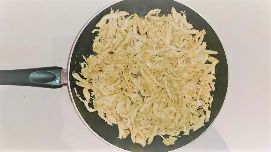 A frying pan full of cooked shredded chicken pieces