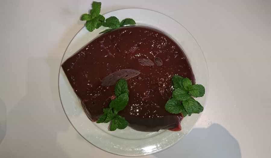 a large chunk of raw beef liver on a plate with some decorative mint herb