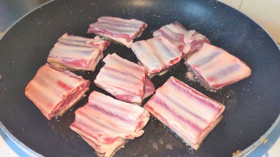 lamb rib pieces being fried in a pan