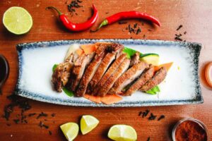 A plate of meat on a table with some chilli and lemon slices around
