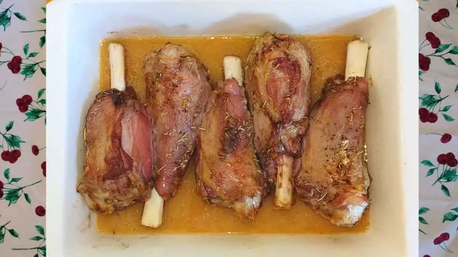 Partially roasted lamb shanks submerged in stock in a roasting dish