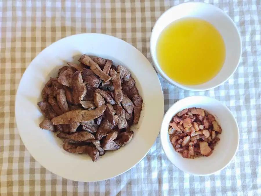 fried liver slices, fried bacon bits and melted tallow on a table